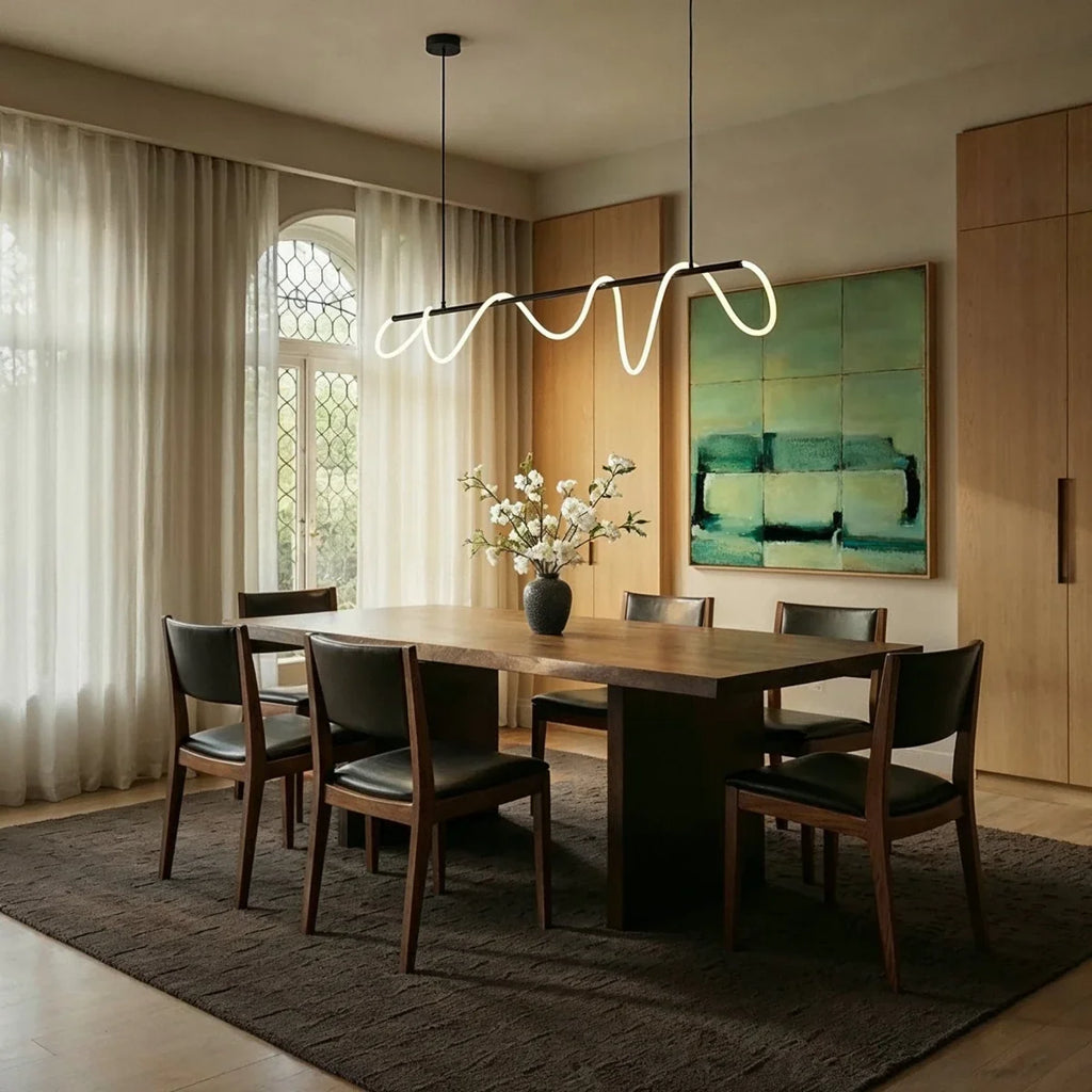Clérachic Linea chandelier in black, glowing warm above a dark wood dining table set with a dark ceramic vase of white blossoms.