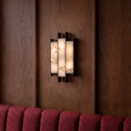 Clérachic wall sconce glowing on dark wood panelling above the ribbed wine-red back of a banquette seat.