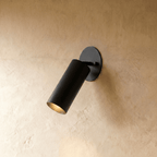 Clérachic wall lamp in matte black, an adjustable cylinder spotlight angled down from an oval plate.