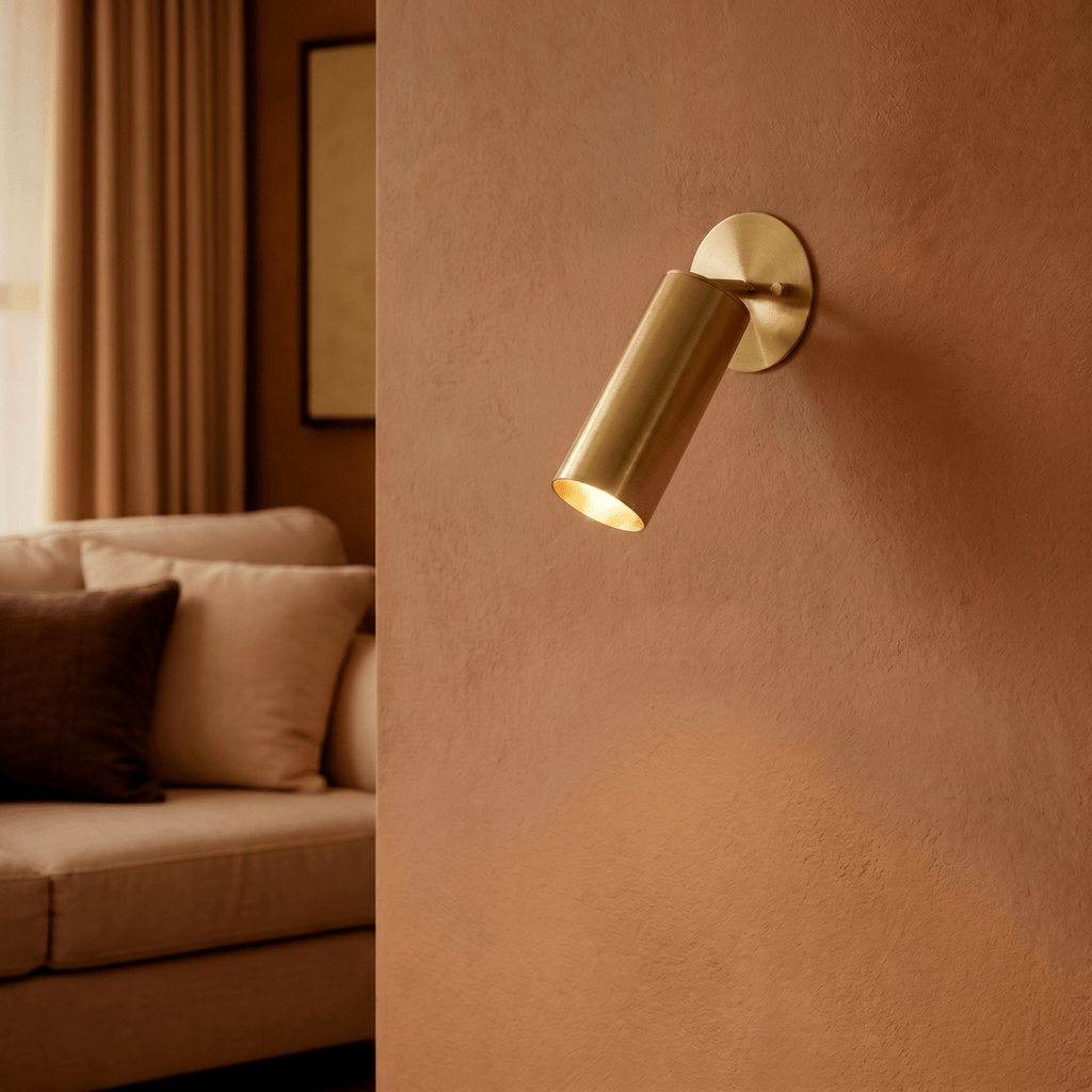 Clérachic wall lamp in brass glowing on a terracotta wall beside a living room sofa and framed art.