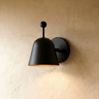 Clérachic wall lamp in matte black, its bell-shaped shade tilted forward on a round wall plate.