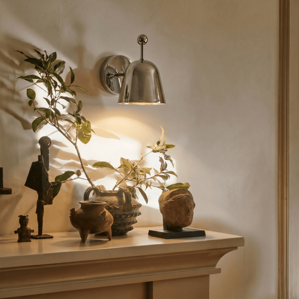 This chrome Clérachic wall lamp lights a mantel styled with small sculptures and potted greenery.