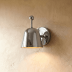 Clérachic wall lamp in polished chrome, its bell shade reflecting light above a plaster wall.