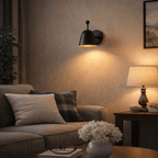A black Clérachic wall lamp lights a sofa corner with plaid pillows and a warm table lamp nearby.