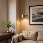 A brass Clérachic wall lamp lights a living room corner beneath a framed black-and-white landscape.