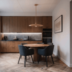 Clérachic brass saucer pendant light glowing above a round dining table in a kitchen with dark wood cabinetry.