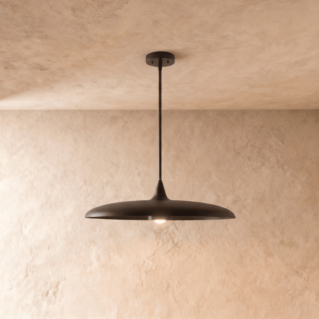 Clérachic pendant light in matte black, its wide saucer shade suspended below a plaster ceiling on a slender rod.