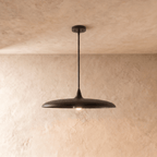 Clérachic pendant light in matte black, its wide saucer shade suspended below a plaster ceiling on a slender rod.