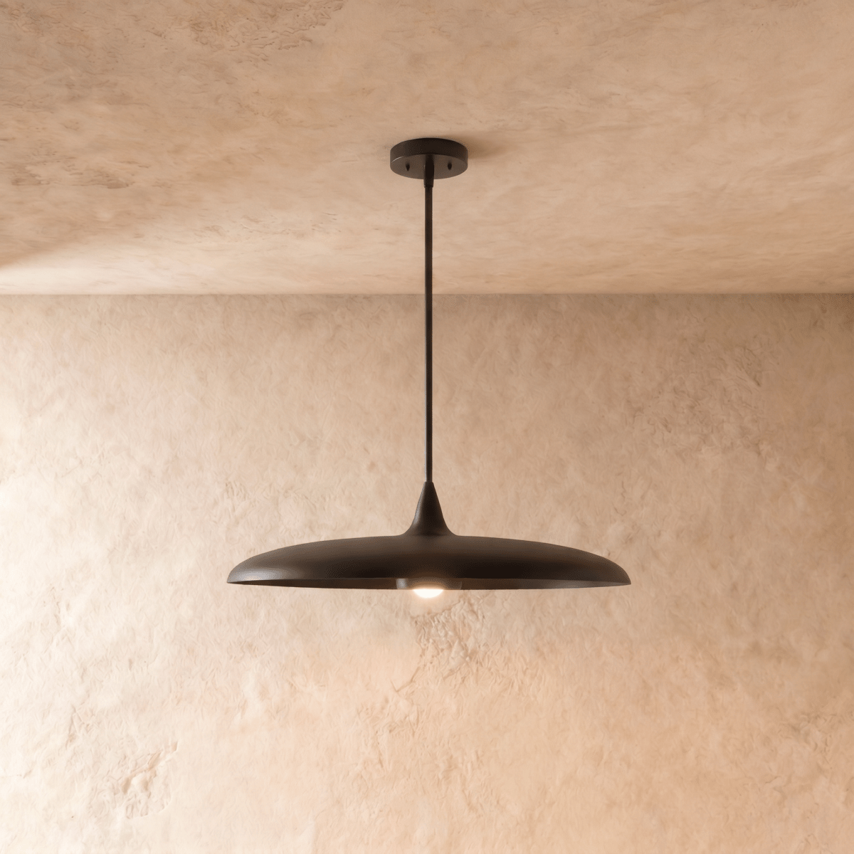 Clérachic pendant light in matte black, its wide saucer shade suspended below a plaster ceiling on a slender rod.