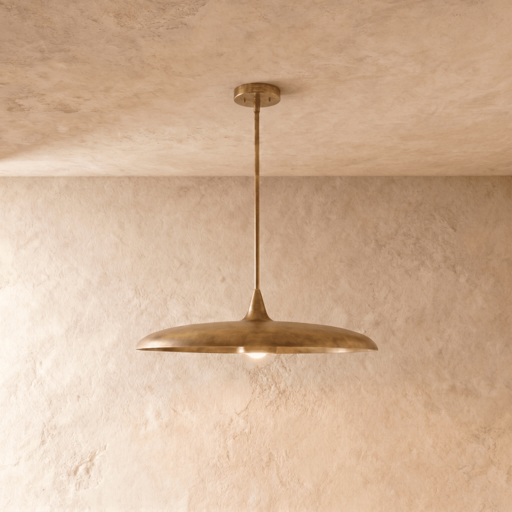 Clérachic pendant light in vintage brass, its wide saucer shade suspended below a plaster ceiling on a slender rod.