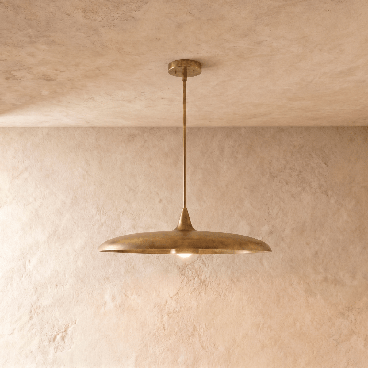 Clérachic pendant light in vintage brass, its wide saucer shade suspended below a plaster ceiling on a slender rod.