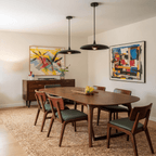 Clérachic matte black saucer pendant lights paired above a walnut dining table flanked by two colourful abstract paintings.