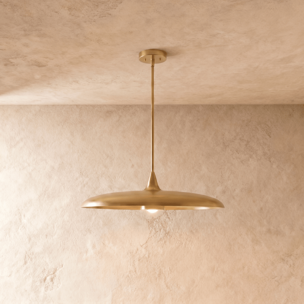 Clérachic pendant light in a brighter brass finish, its wide saucer shade hanging below a plaster ceiling.