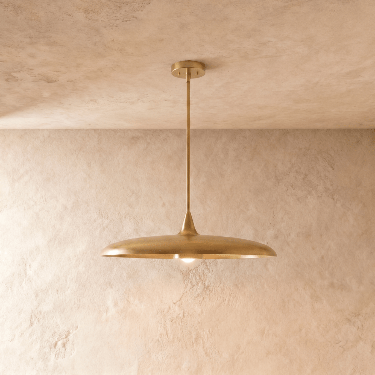Clérachic pendant light in a brighter brass finish, its wide saucer shade hanging below a plaster ceiling.