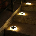 Three paw lights lit along the edge of stone garden steps at night, beside a metal handrail.