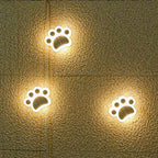 Three paw lights lit warm on beige paving tiles, each throwing a soft circle of light.