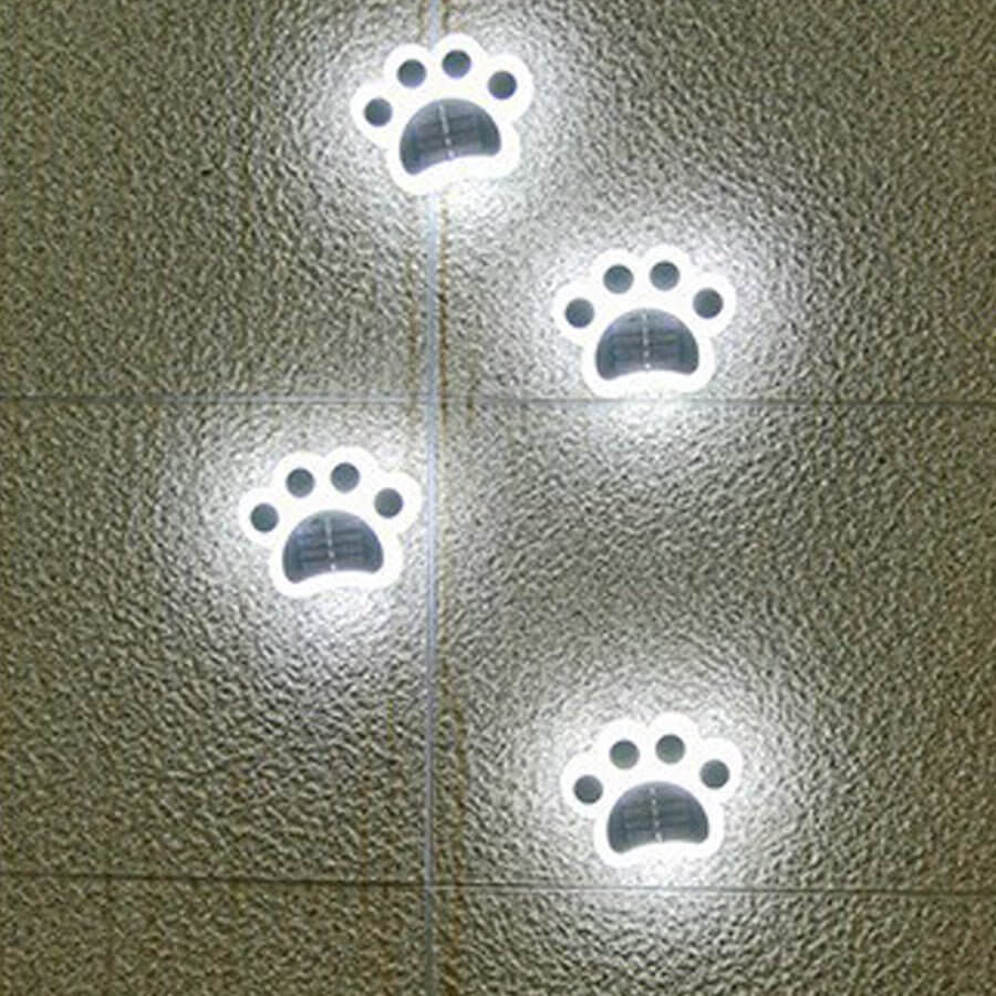 Four paw lights giving a cool white glow across textured grey paving slabs at night.