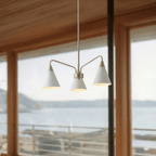 A Clérachic three-arm chandelier hangs before glass doors with a wide view over a coastal inlet.