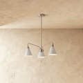 This Clérachic three-arm chandelier hangs against a plaster wall, its cone shades finished in soft white.