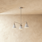 This Clérachic three-arm chandelier hangs against a plaster wall, its cone shades finished in soft white.