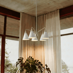 This Clérachic five-arm chandelier glows warmly in a curtained corner beside a large potted monstera.
