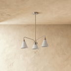A Clérachic chandelier with three white cone shades hangs from a slim rod against a textured plaster wall.