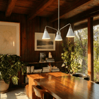A Clérachic three-arm chandelier lights a wood-beamed dining table in a home overlooking the water.