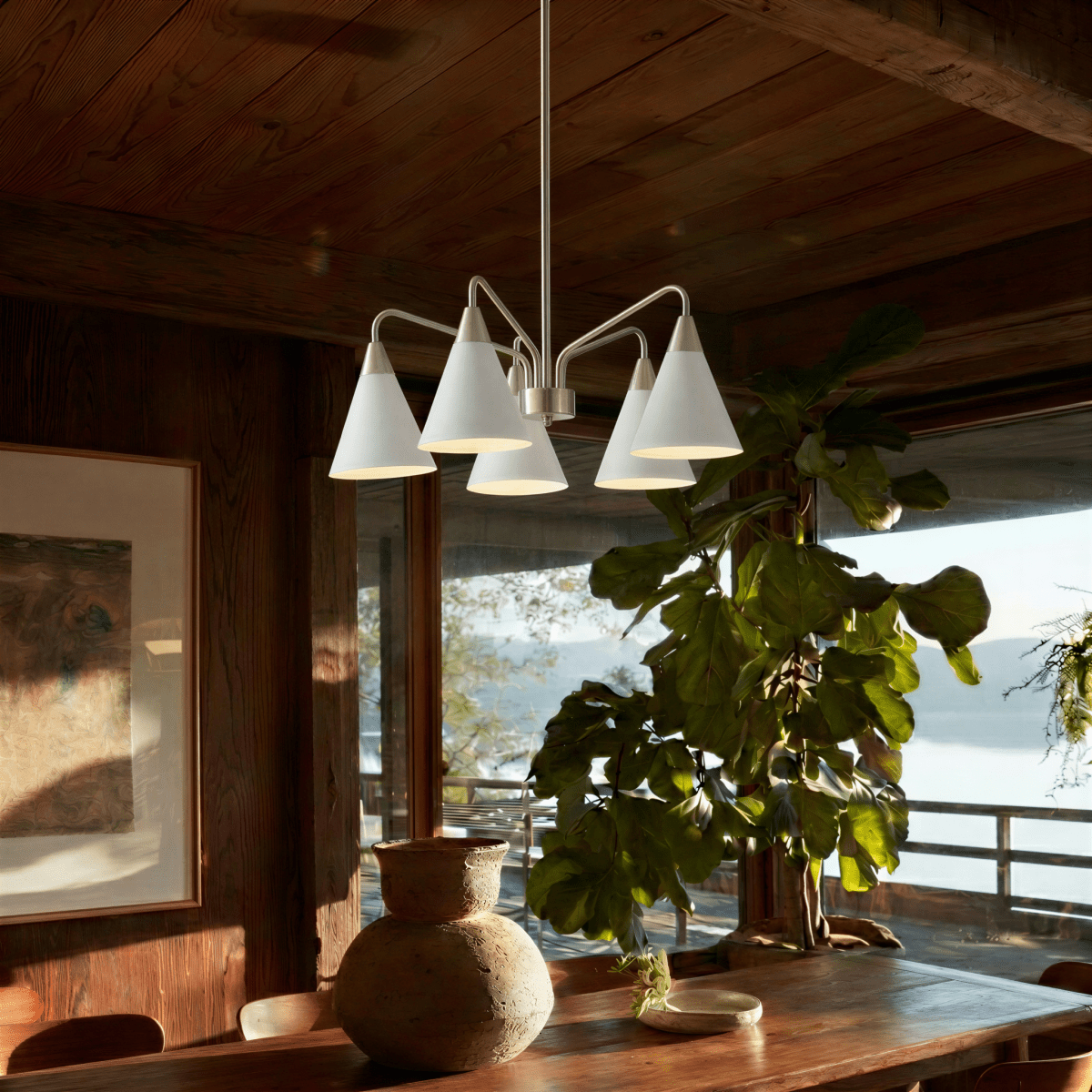 This Clérachic five-arm chandelier glows warmly above a wooden dining table beside a leafy potted plant.