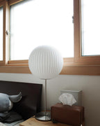 Faux silk bubble table lamp with chrome stem lit warmly on a side table
