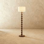 Clérachic stacked-sphere wood floor lamp in a dark walnut finish, its cream drum shade lit against a plain plaster backdrop.