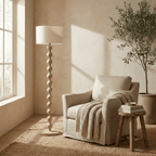 Clérachic stacked-sphere wood floor lamp in a pale wood finish, unlit in a sunlit living room beside a linen armchair and a potted olive tree.