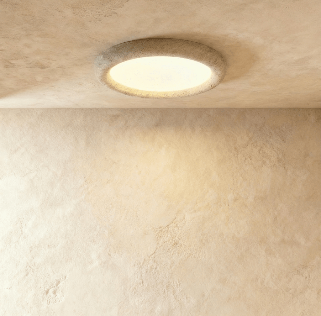 Clérachic stone ring ceiling light seen from below at an angle, its speckled ring standing proud of the ceiling above a soft pool of light.
