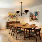 Clérachic matte black chandelier hanging above a walnut dining table flanked by two colourful abstract paintings.