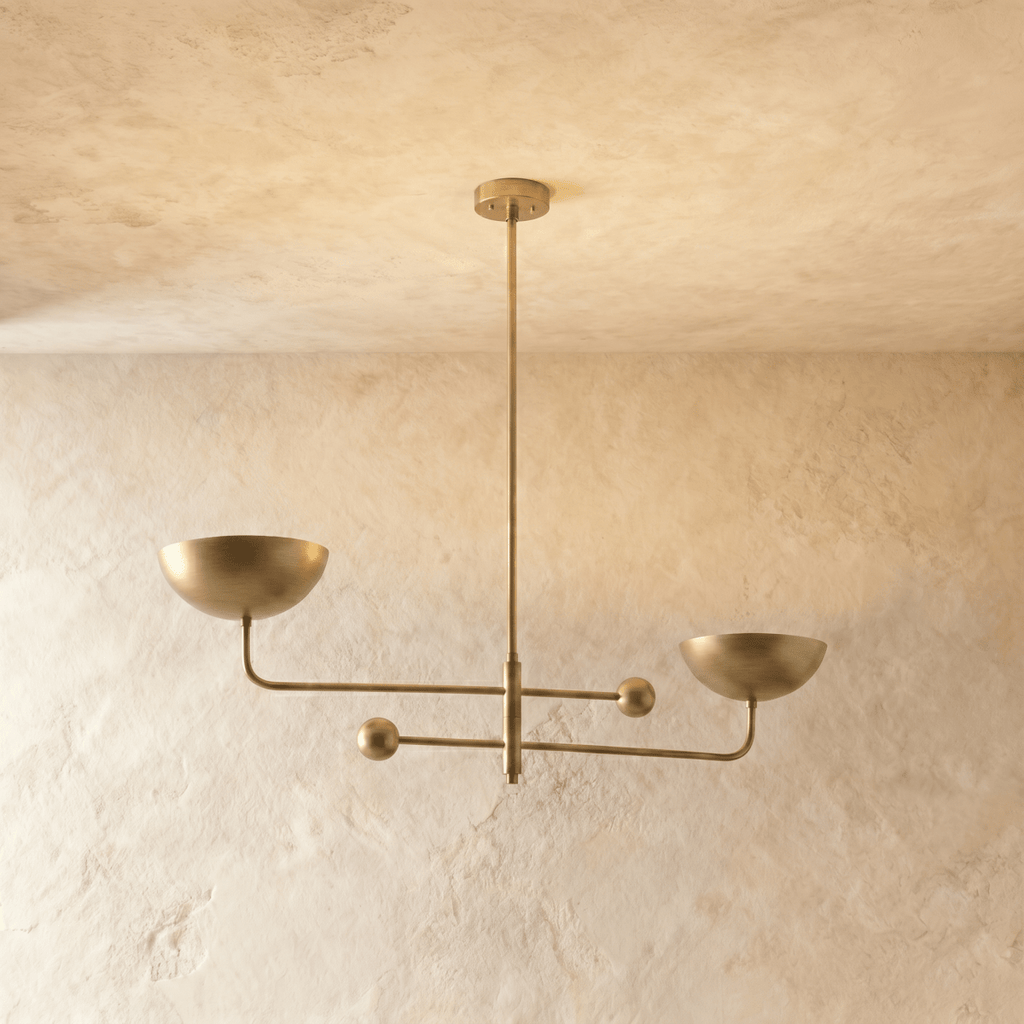Clérachic chandelier in a brighter brass finish, its two balanced arms and bowl shades against a plaster ceiling.