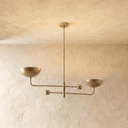 Clérachic chandelier in a brighter brass finish, its two balanced arms and bowl shades against a plaster ceiling.