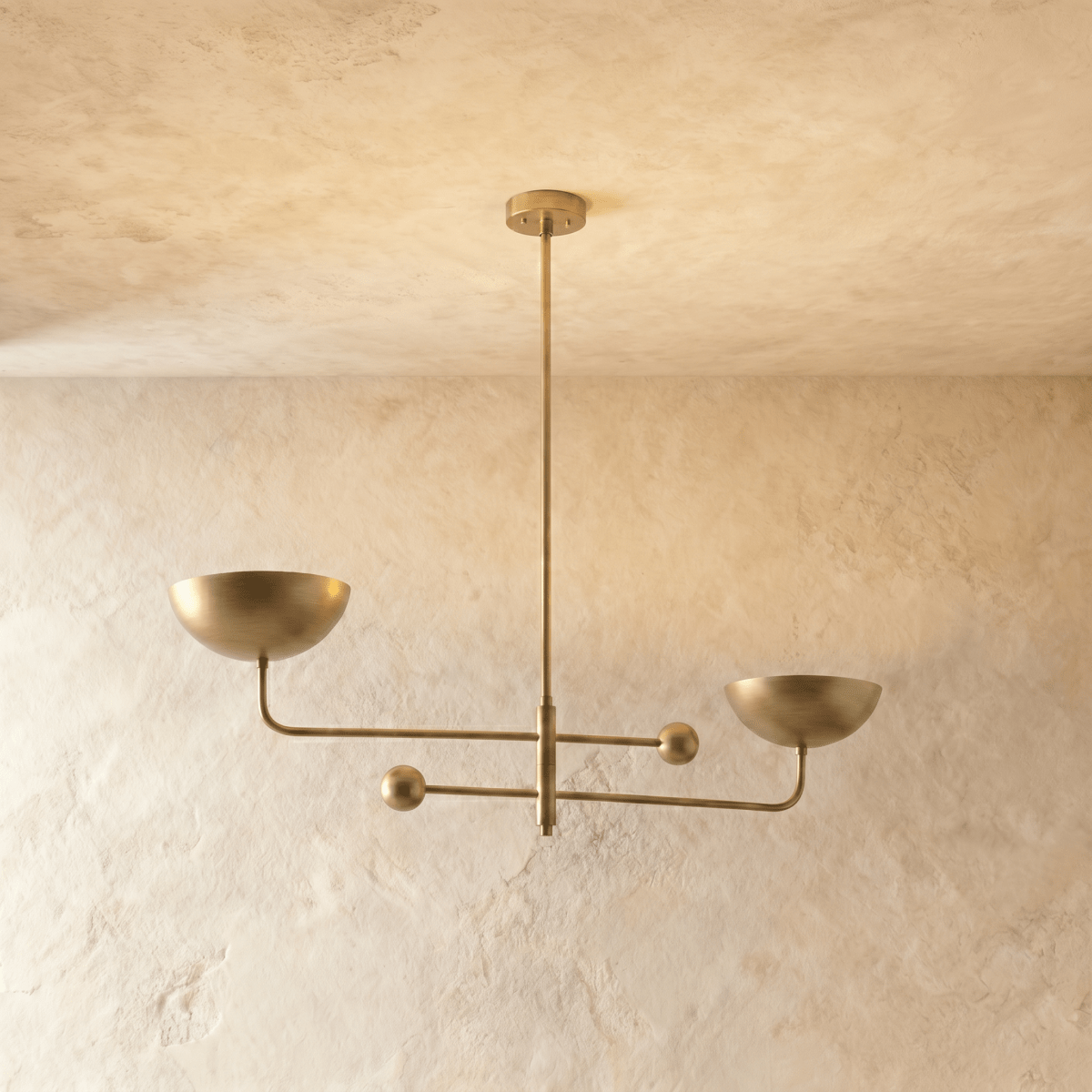 Clérachic chandelier in a brighter brass finish, its two balanced arms and bowl shades against a plaster ceiling.