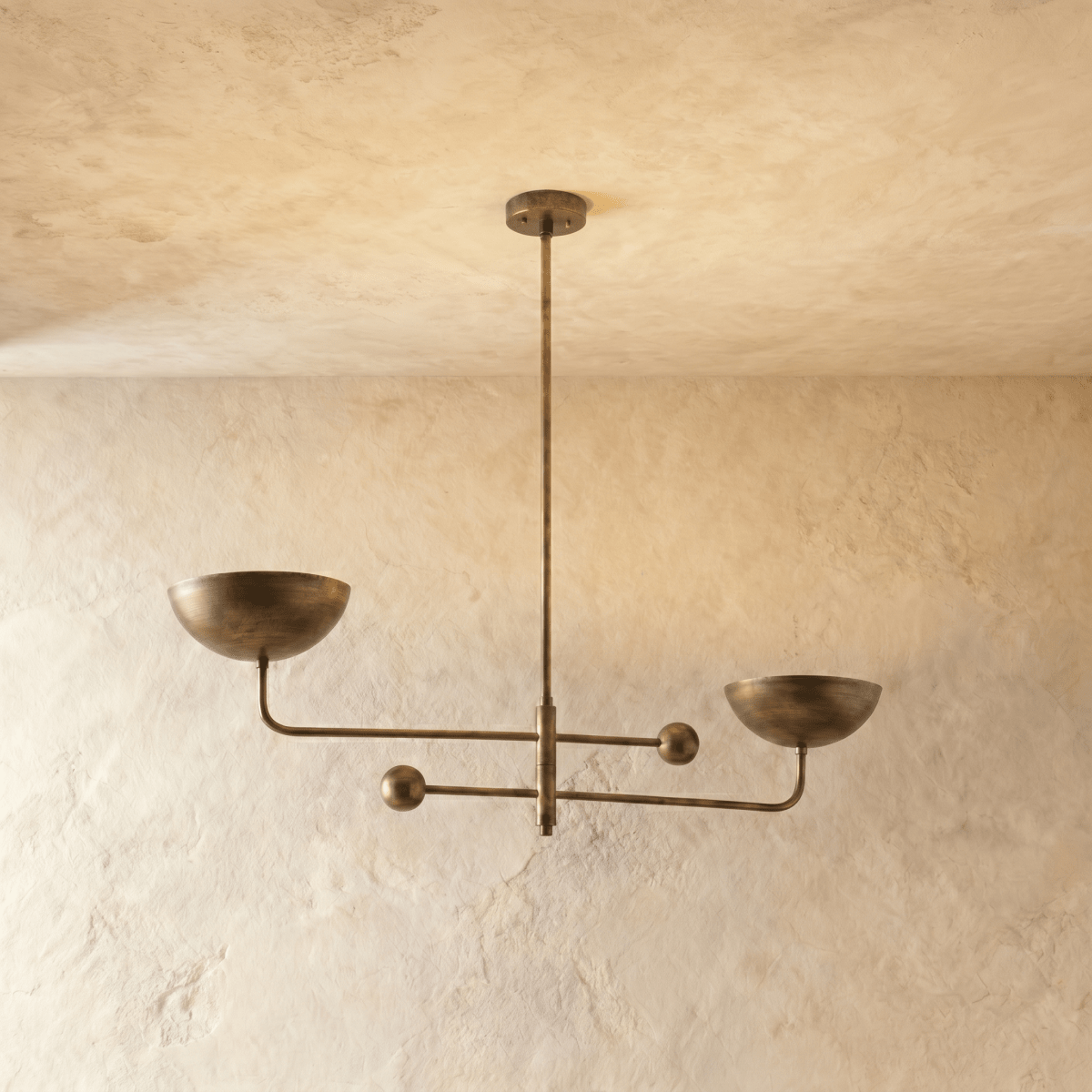 Clérachic chandelier in vintage brass, its two balanced arms and bowl shades hung from a plaster ceiling.
