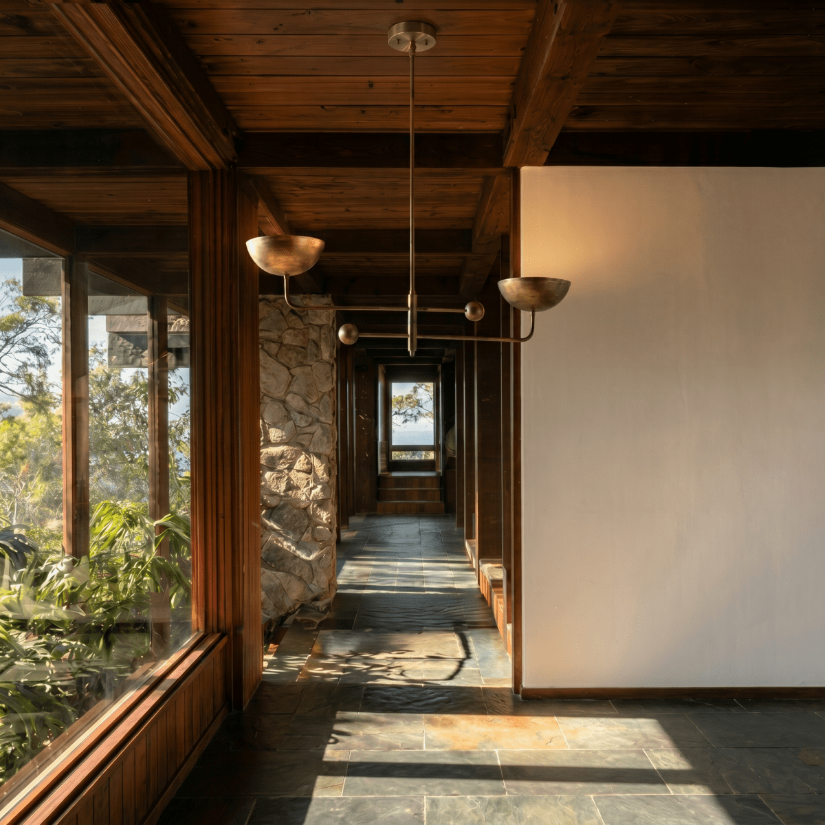 Clérachic vintage brass chandelier hanging in a stone-and-timber hallway overlooking hills through a window.