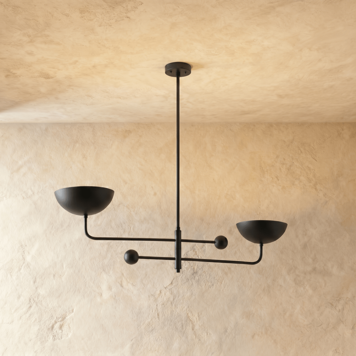 Clérachic chandelier in matte black, its two balanced arms and bowl shades hung from a plaster ceiling.