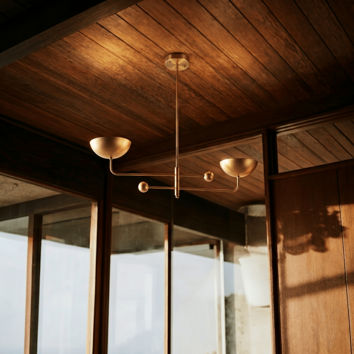Clérachic vintage brass chandelier mounted below a timber-panelled ceiling beside floor-to-ceiling glass doors.