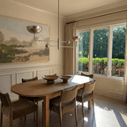 Clérachic chrome chandelier hanging above an oval dining table beside a landscape painting and garden windows.