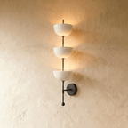Clérachic three-tier bowl sconce in matte black with white glass shades, mounted on a plaster wall in studio light.