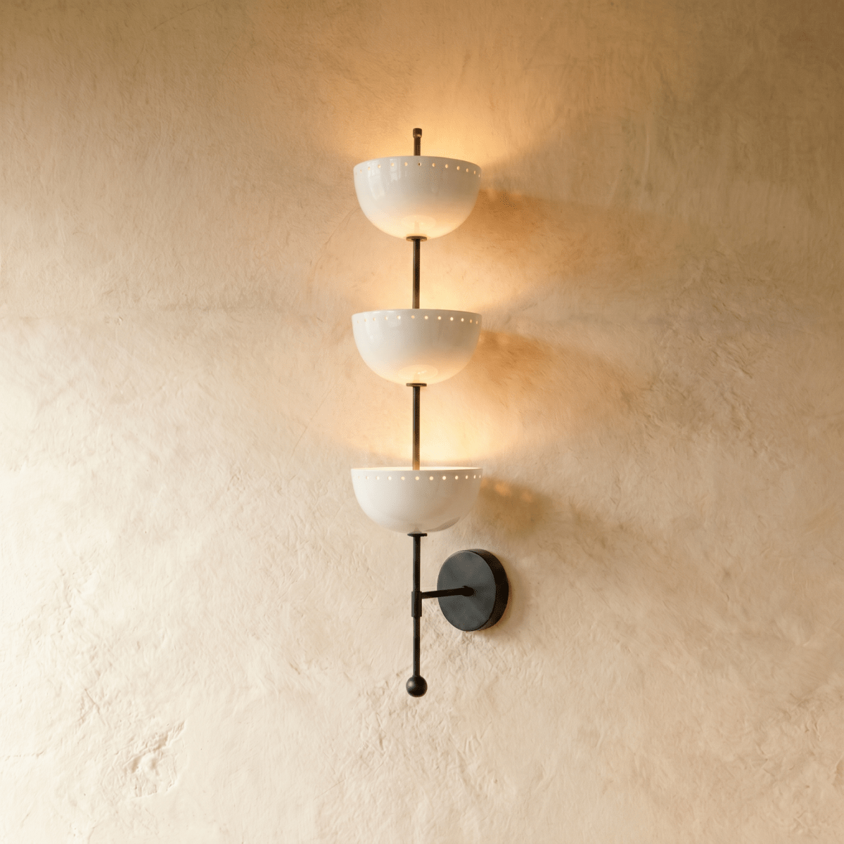 Clérachic three-tier bowl sconce in matte black with white glass shades, mounted on a plaster wall in studio light.