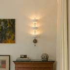 Clérachic brass three-tier bowl sconce lit beside a framed abstract painting above a wooden sideboard.