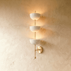 Clérachic three-tier bowl sconce in polished brass with white glass shades, mounted on a plaster wall in studio light.