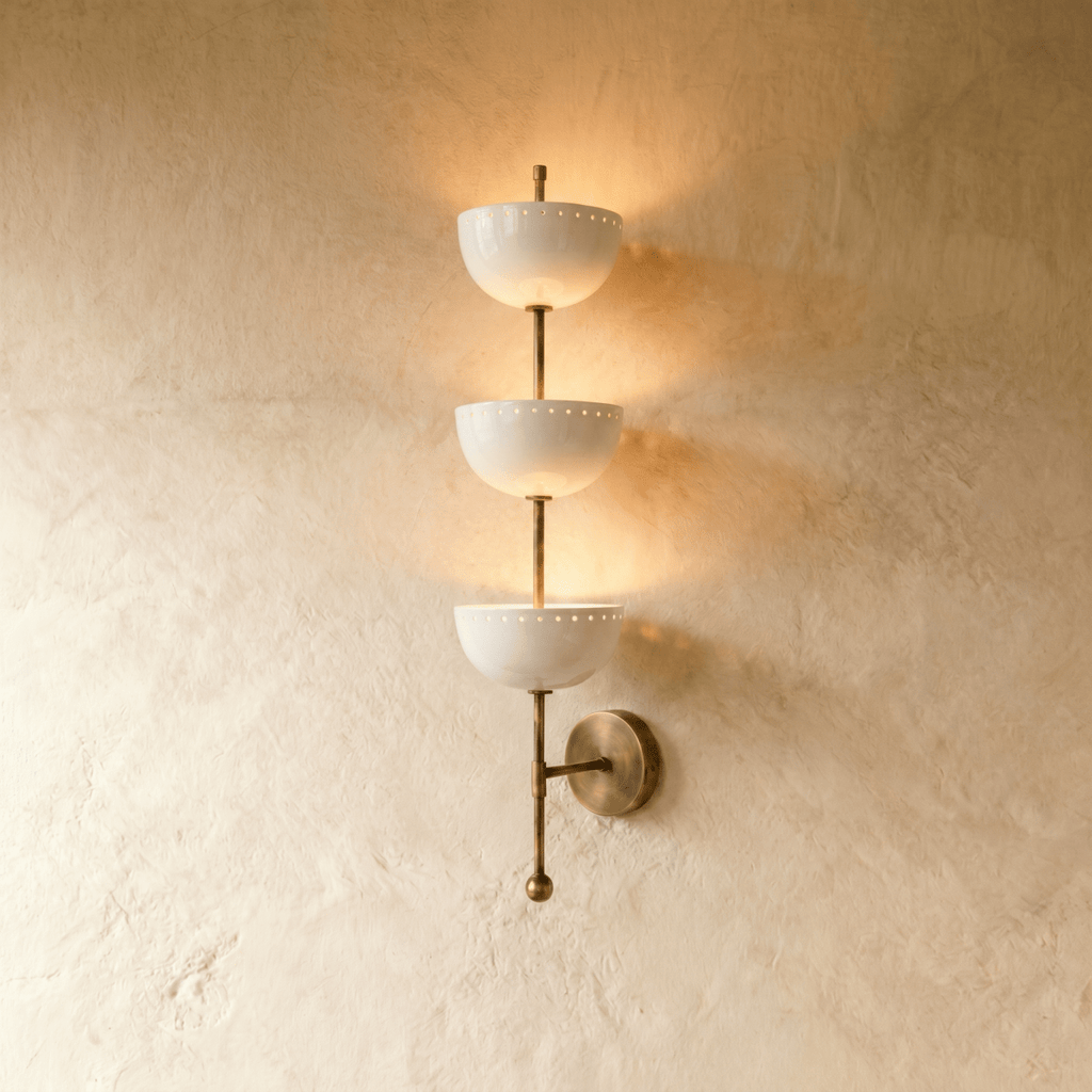 Clérachic three-tier bowl sconce in vintage brass with white glass shades, mounted on a plaster wall in studio light.