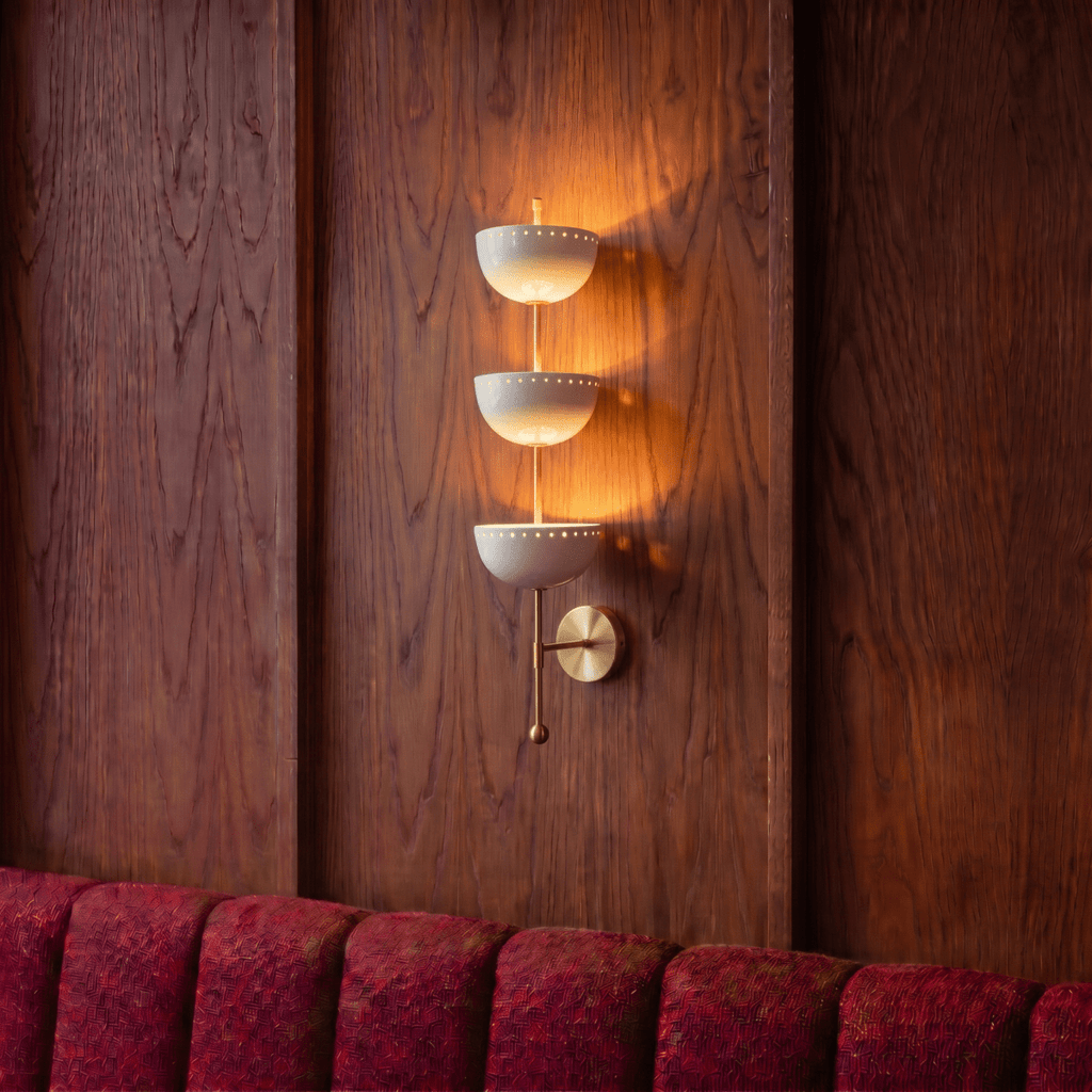 Clérachic vintage brass three-tier bowl sconce lit against a wood-panelled wall above a red velvet banquette.