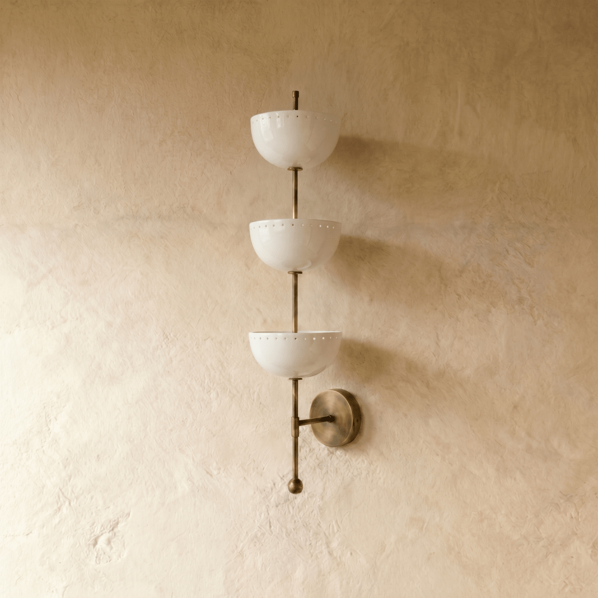 Clérachic three-tier bowl sconce in vintage brass, shown from a slightly closer studio angle on a plaster wall.