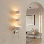Clérachic chrome three-tier bowl sconce lit on a hallway wall beside an archway into a living room.