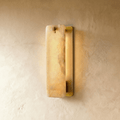 Clérachic marble wall sconce in a copper-tone finish, lit on a warm plaster wall and seen at an angle, so the open metal channel behind the stone shows its glowing inner wall.